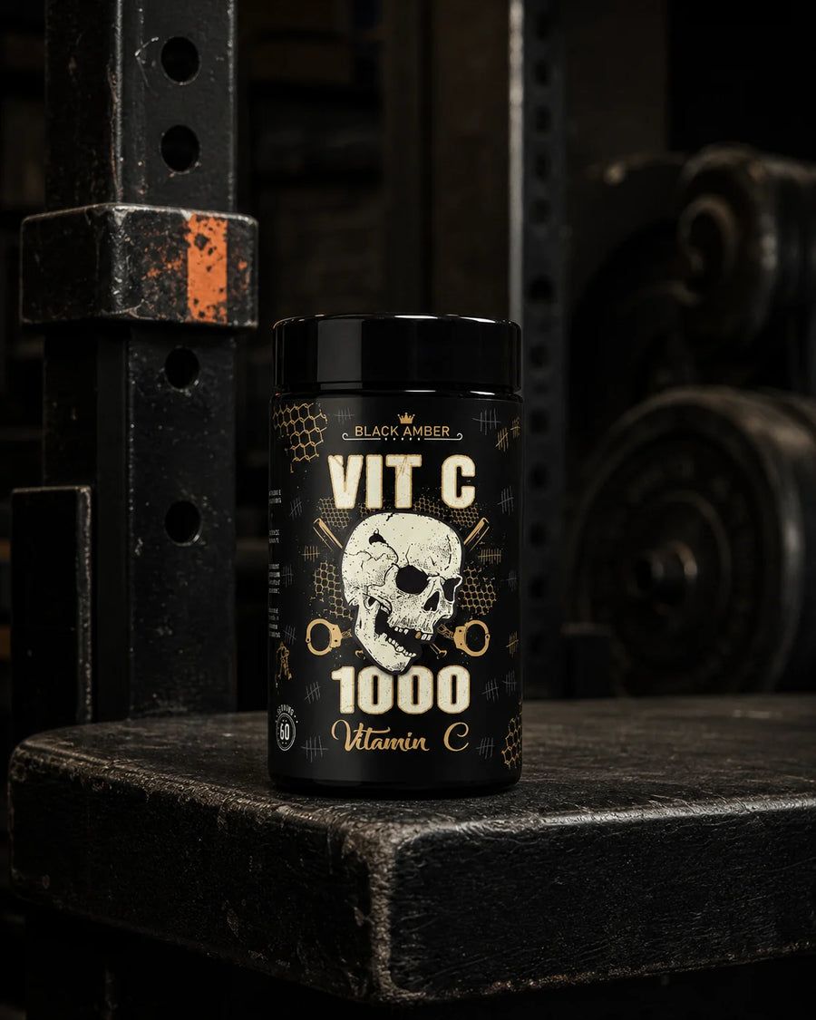 Black Amber Vitamin C 1000 bottle on a worn black platform beside an iron squat rack