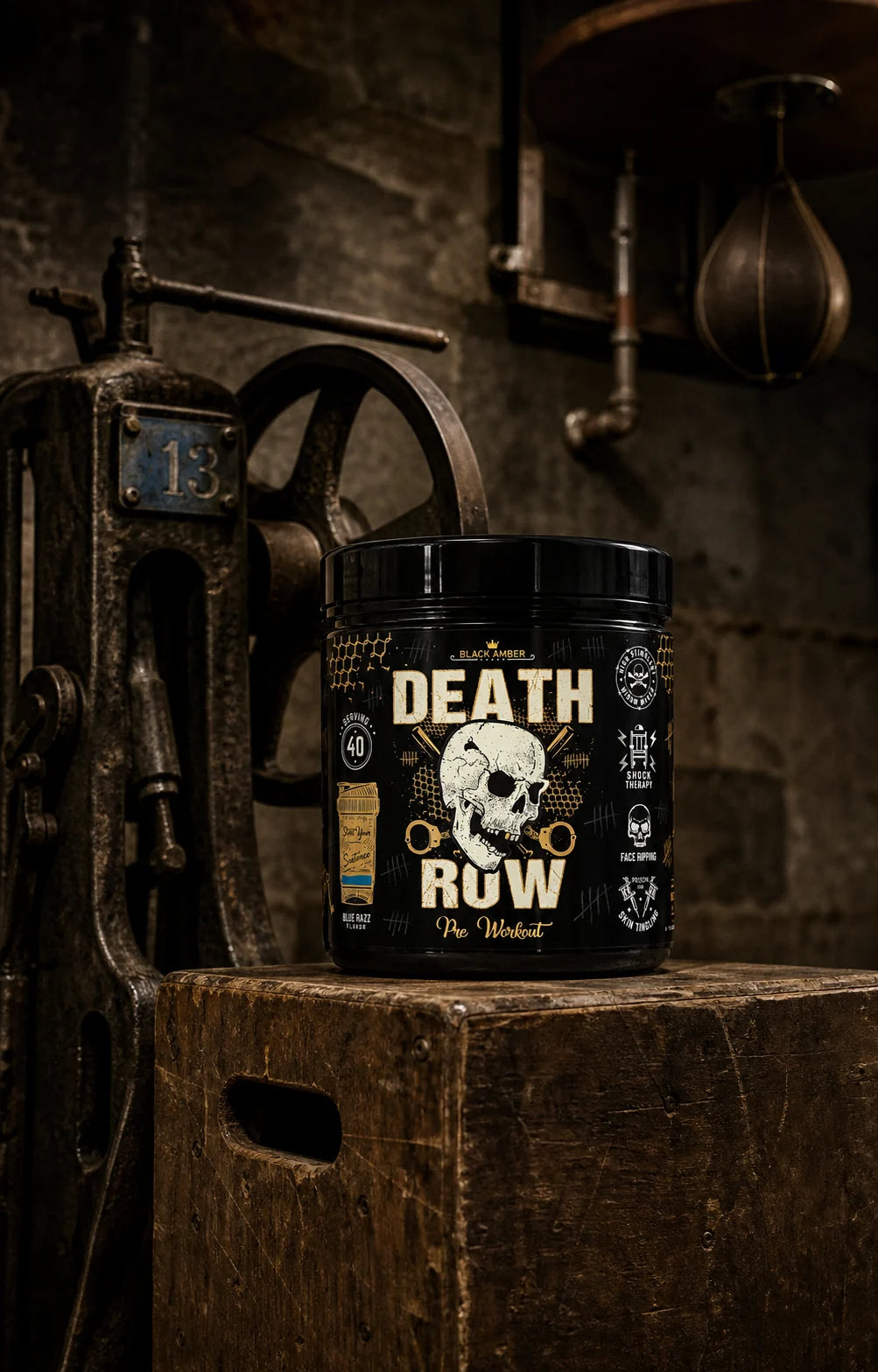 Black Amber Death Row Blue Razz pre-workout tub on a wooden training box beside a hand-crank machine and leather speed bag